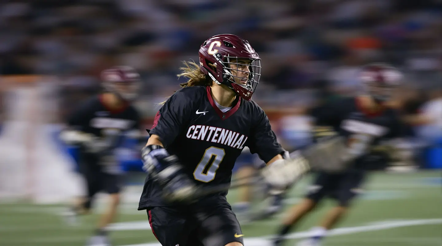 lacrosse player running in a game with a red helmet and a black uniform